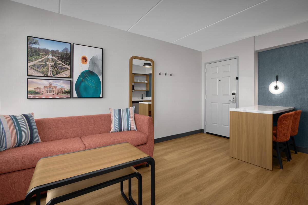 A modern room with a sofa, a small table, a desk with chairs, and framed pictures on the wall.