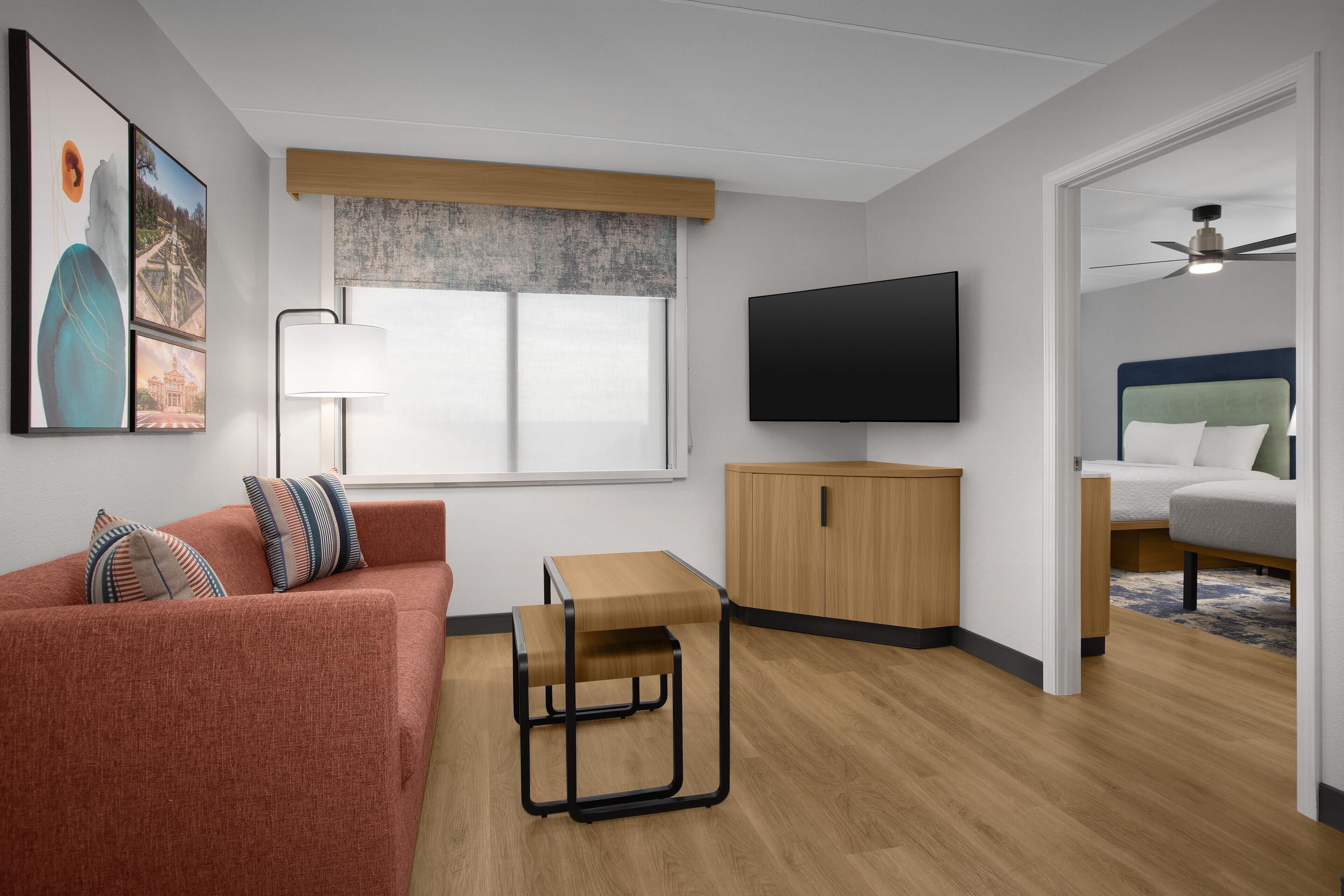 A modern living room with a sofa, a small wooden table, a TV, and a ceiling fan.