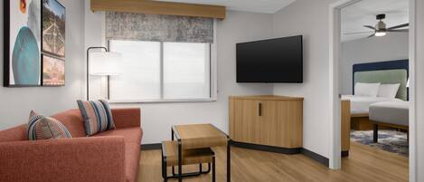 A modern living room with a sofa, a small wooden table, a TV, and a ceiling fan.