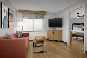 A modern living room with a sofa, a small wooden table, a TV, and a ceiling fan. - Homewood Suites by Hilton Ft. Worth-North at Fossil Creek (Fort Worth)