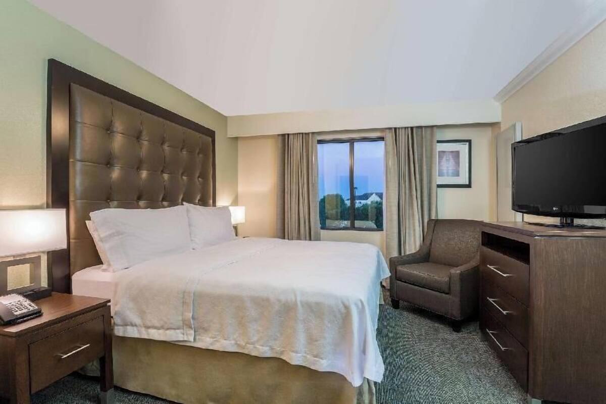A hotel room with a large bed, a desk, a chair, a television, and a window with a view.
