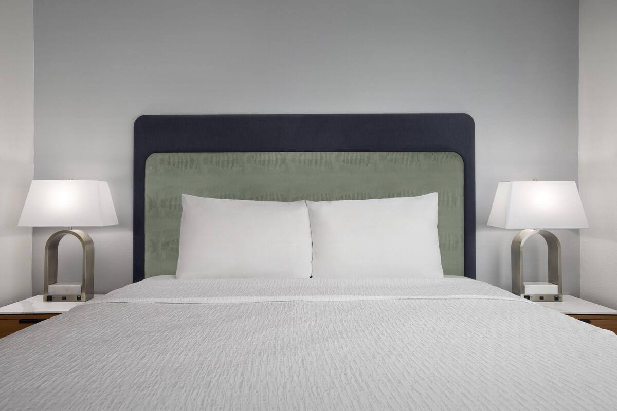 A neatly made bed with white linens, a dark headboard, and two bedside lamps on either side.