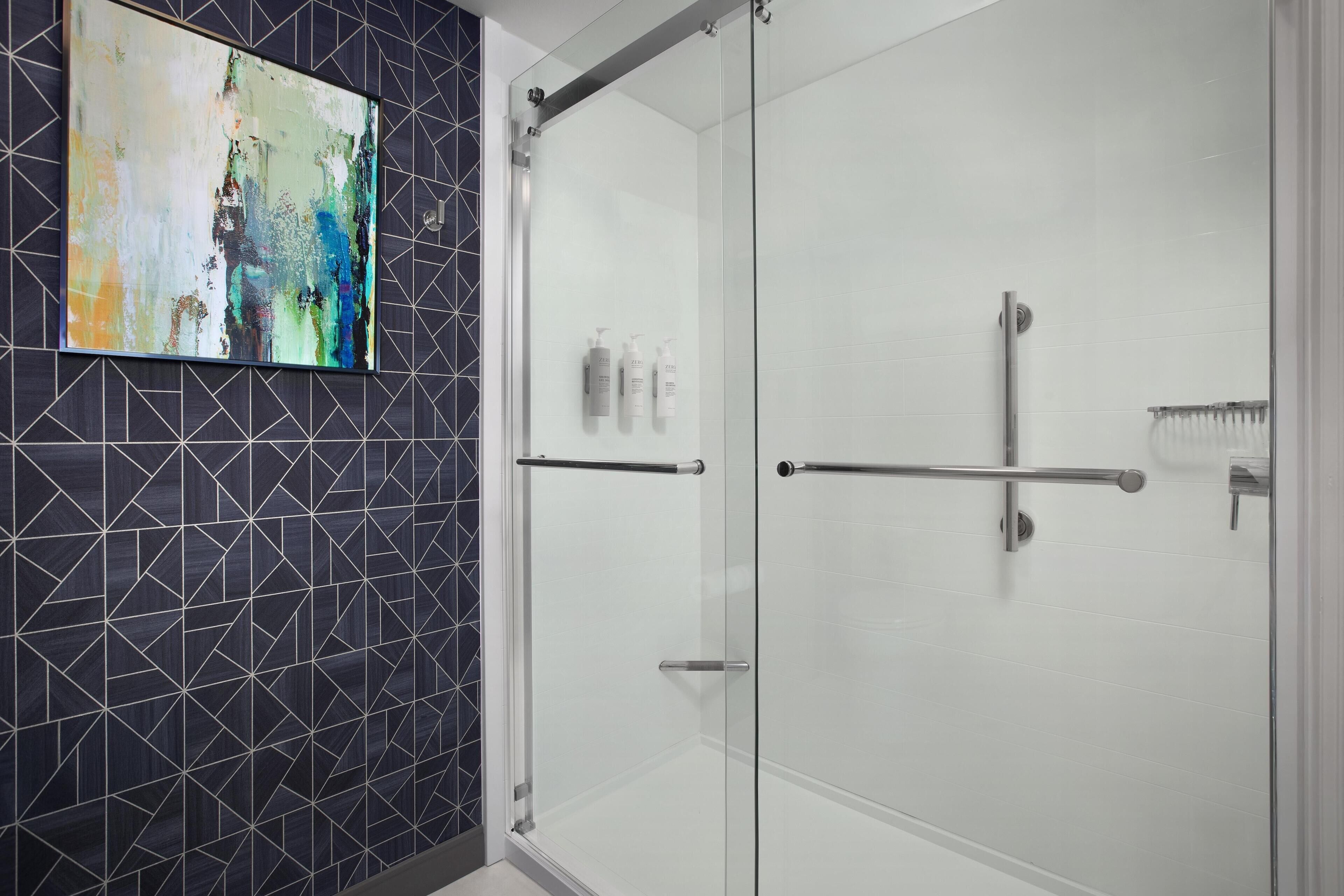 Un baño moderno con cabina de ducha de vidrio, un rebozo de azulejos geométricos y un cuadro abstracto colgado en la pared.