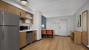 A modern kitchen with stainless steel appliances, wooden cabinets, and a dining area with two chairs. - Homewood Suites by Hilton Ft. Worth-North at Fossil Creek (Fort Worth)