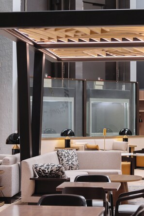 A modern interior with a sofa, tables, and chairs, a glass partition, and a ceiling with a geometric design.