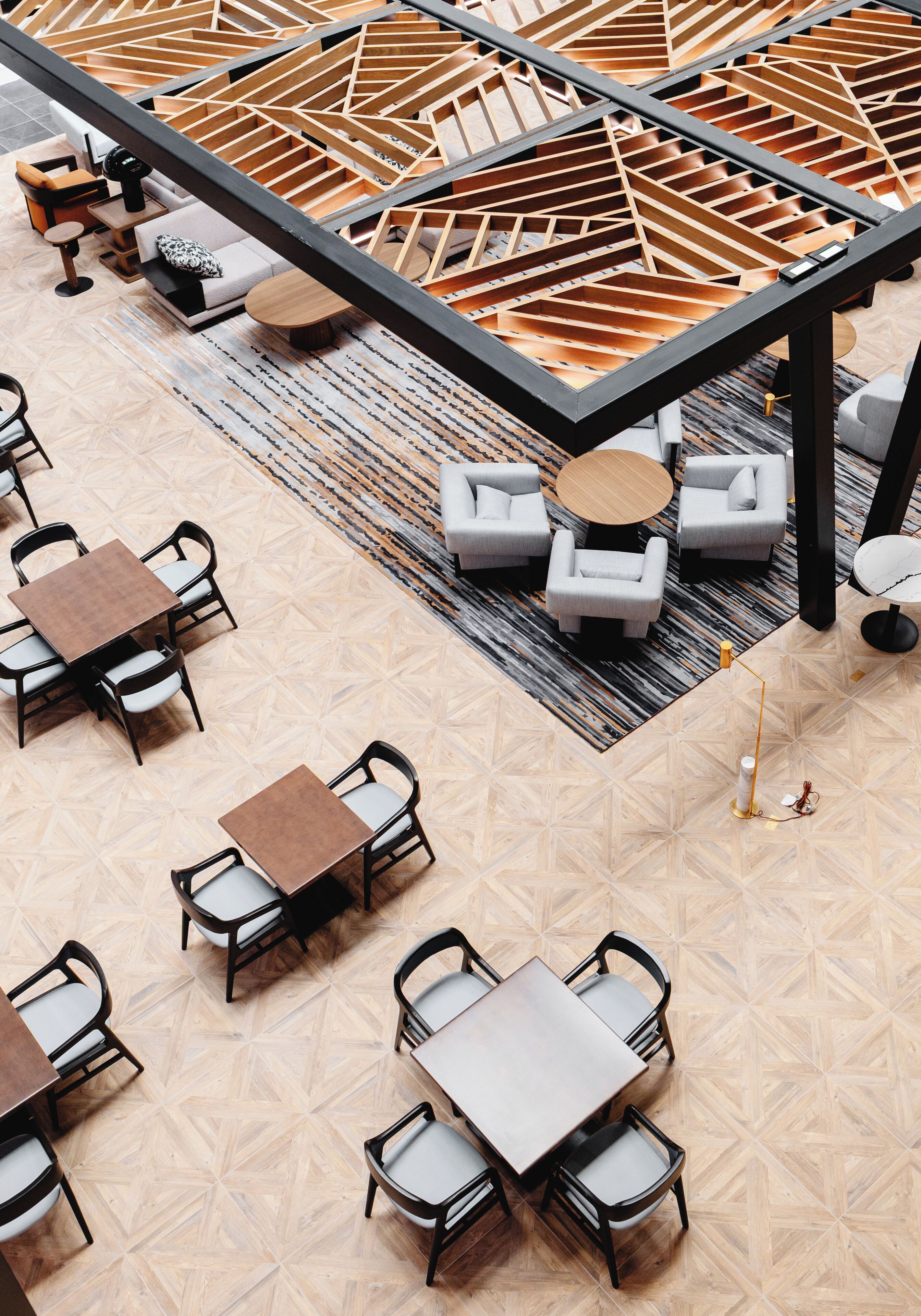 A modern hotel lobby with geometric patterned flooring, a central wooden structure, and seating arrangements including sofas and tables.