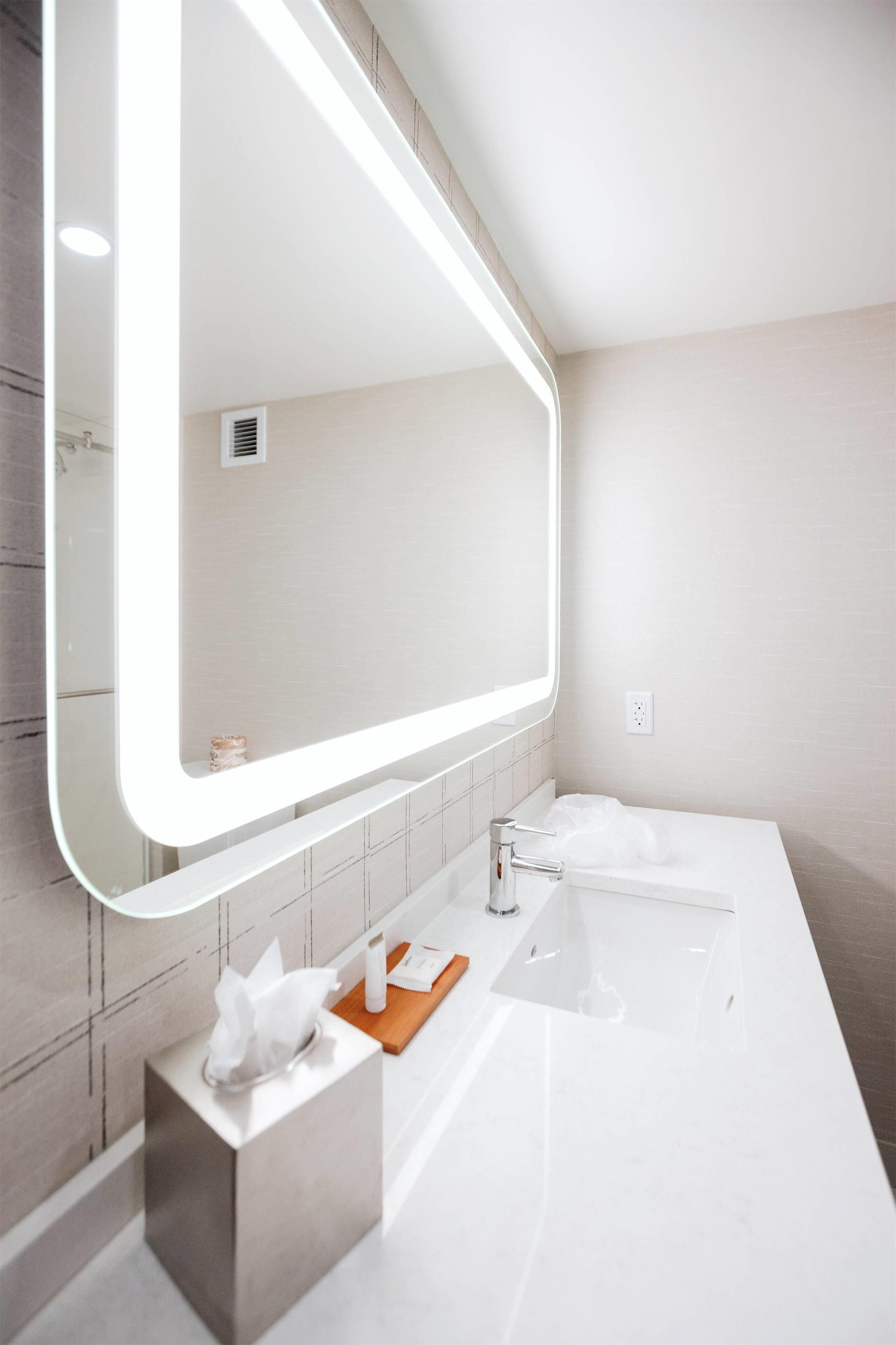 Un baño moderno con un espejo grande, un lavamanos blanco y un mueble de tocador con una caja de pañuelos.