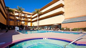 A hotel pool area with multiple levels of balconies, lounge chairs, and a clear blue pool.