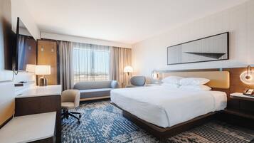Una habitación de hotel con cama, escritorio, silla y un ventanal grande.