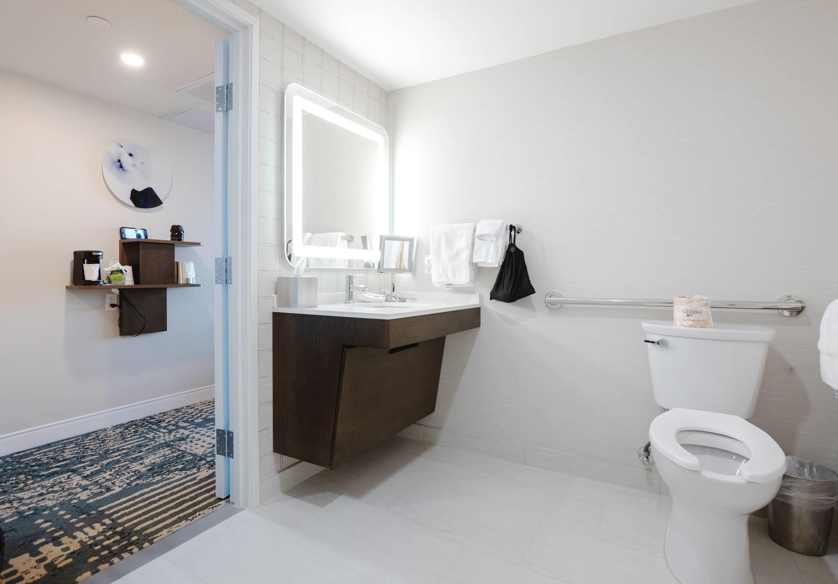 A modern bathroom with a white toilet, a large mirror, a dark wooden vanity, and a glass shower enclosure.