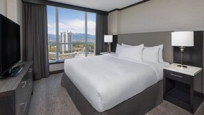 Habitación de hotel con una cama grande, dos mesitas de noche, un televisor y vistas a la ciudad con montañas.