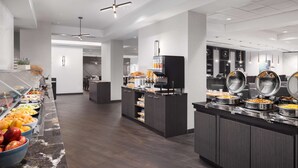 Un área de desayuno de hotel moderna, con mostrador de mármol, bufé de frutas y cereales, y una estación de café.