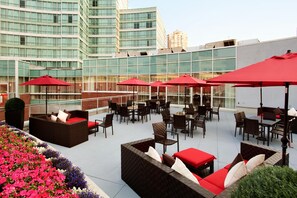 Terraza en la azotea con mobiliario exterior, incluyendo sofás y mesas, rodeada de sombrillas rojas.