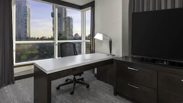 A hotel room with a large window, a desk, a chair, a TV, and a cabinet.