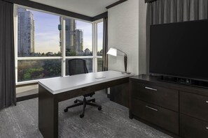 Habitación de hotel con un ventanal grande, un escritorio, una silla, un televisor y un armario.