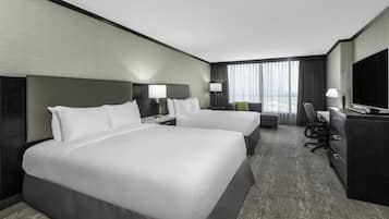 A hotel room with two beds, a desk with a chair, a TV, and a large window with curtains.