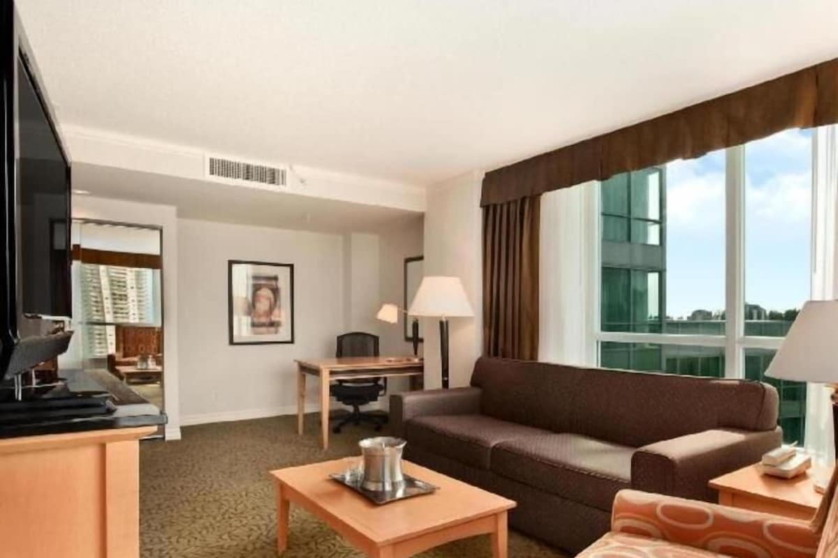 A hotel room with a sofa, armchair, desk, and a television.