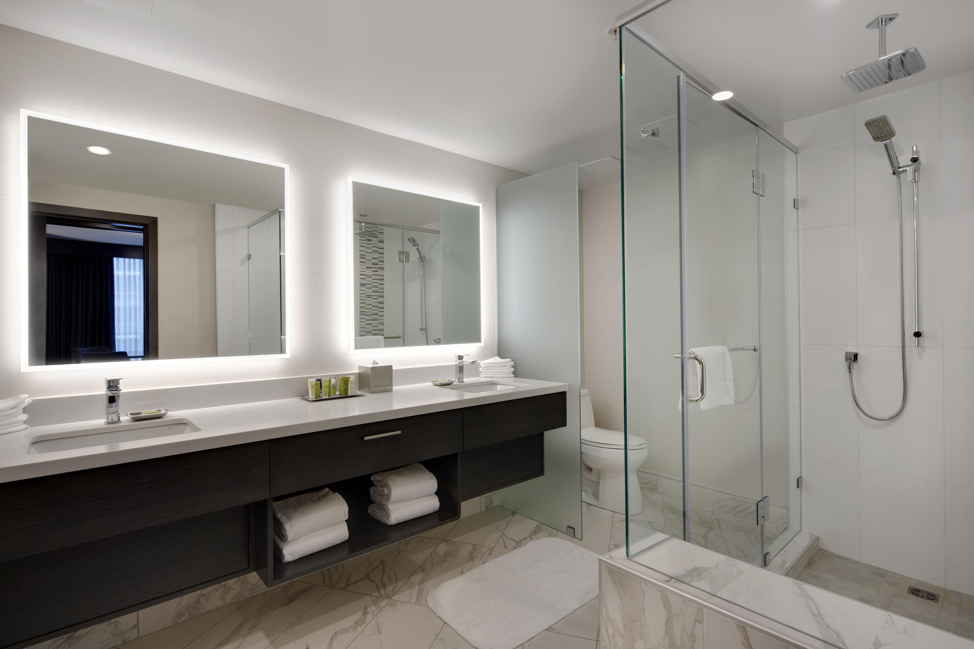 A modern bathroom with a glass-enclosed shower, a large mirror, and a vanity with a dark cabinet.