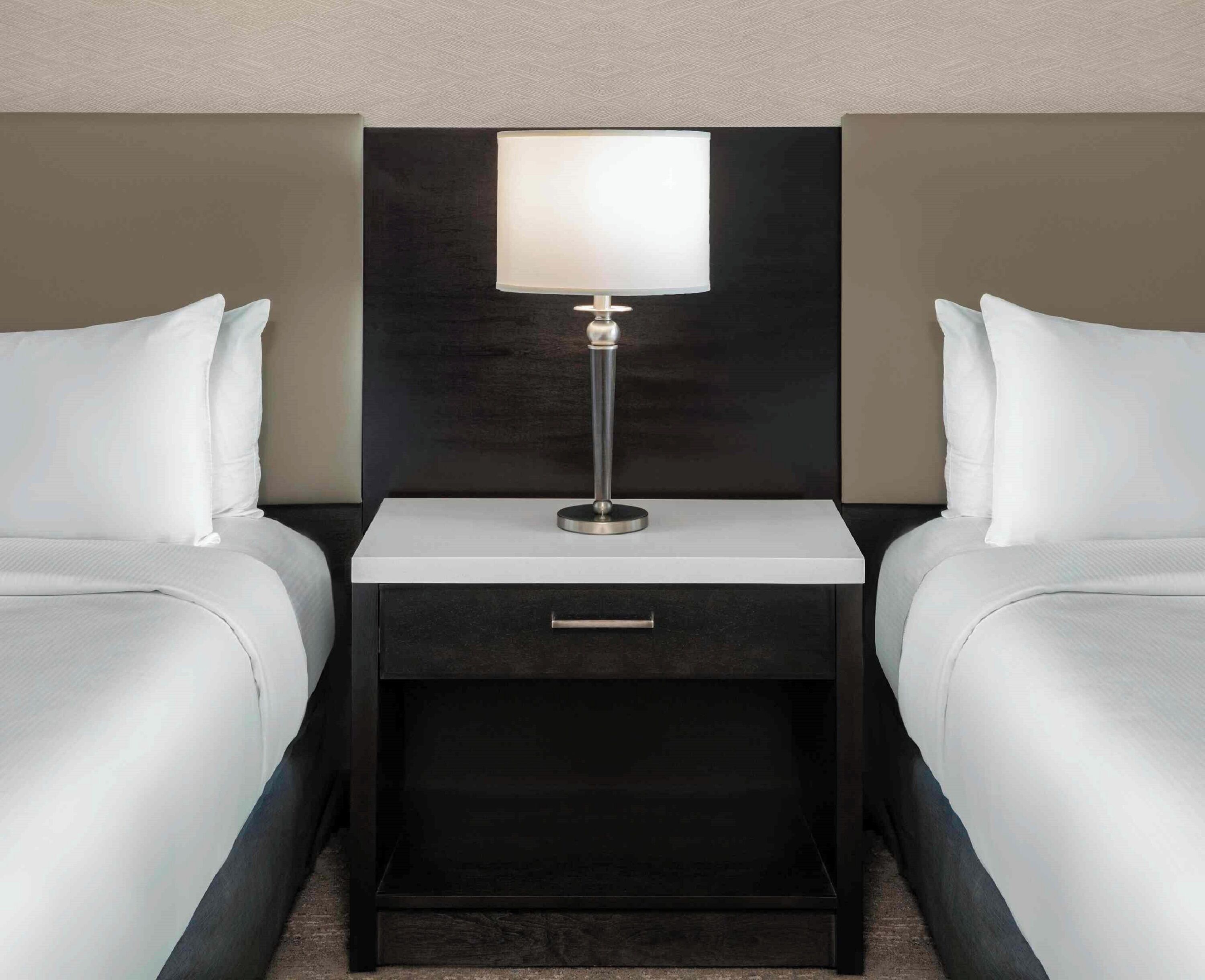 A hotel room with two beds, a nightstand with a lamp, and a drawer.