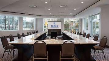 A conference room with a long table, chairs, a screen, and large windows.