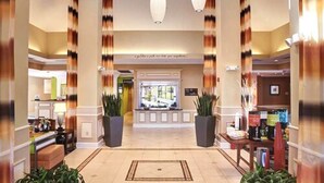 A hotel lobby with a reception desk, large potted plants, and a tiled floor. - Hilton Garden Inn Cleveland Airport (Cleveland)