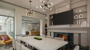 A modern living room with a large white table, comfortable seating, a fireplace, a flat-screen TV, and decorative shelves. - Hilton Garden Inn Cleveland Airport (Cleveland)