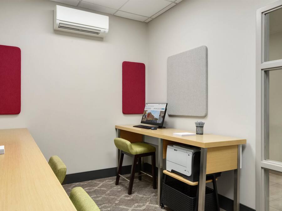 A conference room with a long table, two chairs, a desk with a computer, and two soundproof panels on the walls.