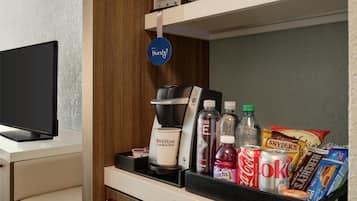 Un minibar con una cafetera, una botella de Coca-Cola, una lata de Diet Coke, una botella de Welch's, una bolsa de Reese's y una caja de detergente Tide.