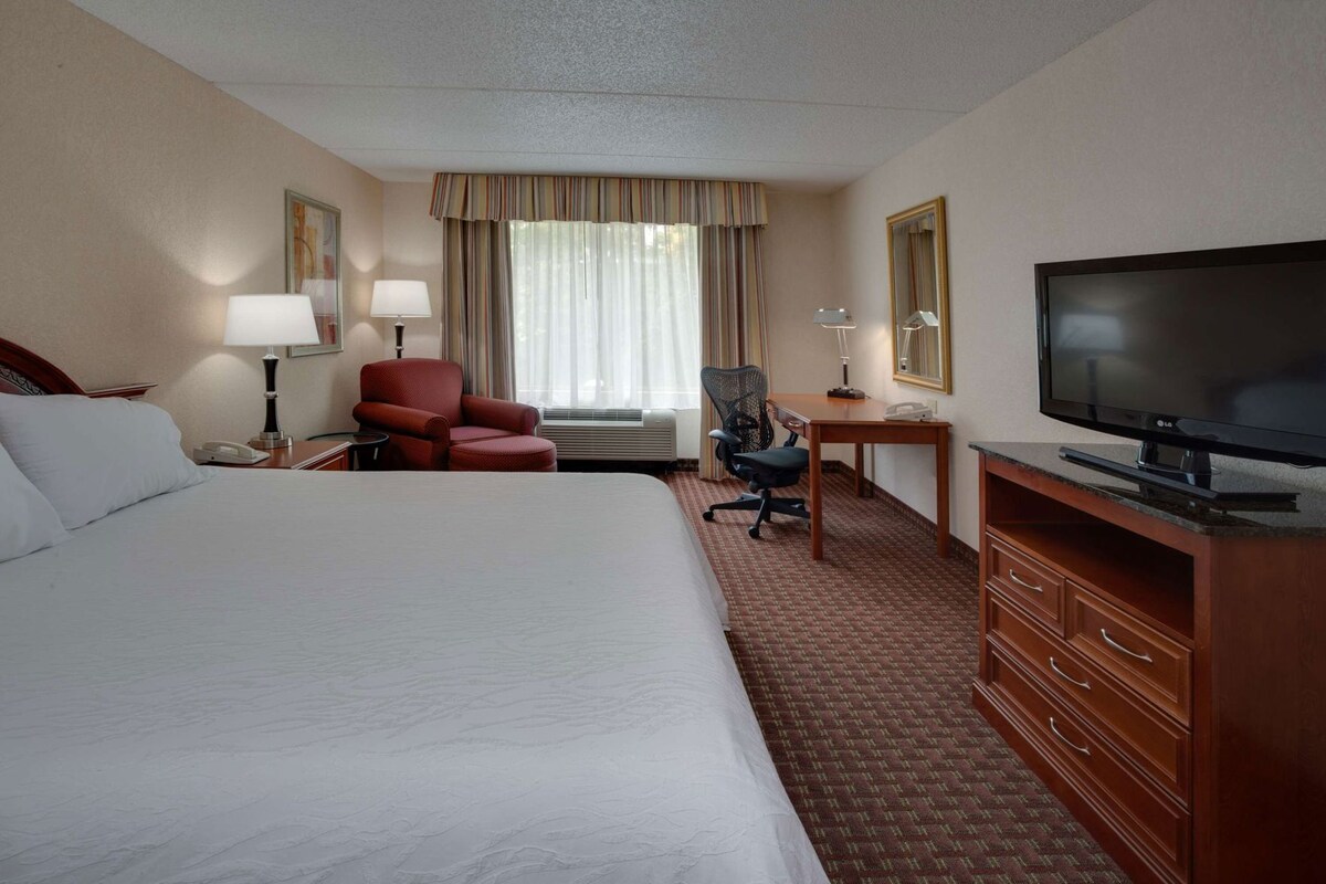 Une chambre d’hôtel avec un grand lit, un bureau avec une télévision, une chaise et une lampe de bureau.