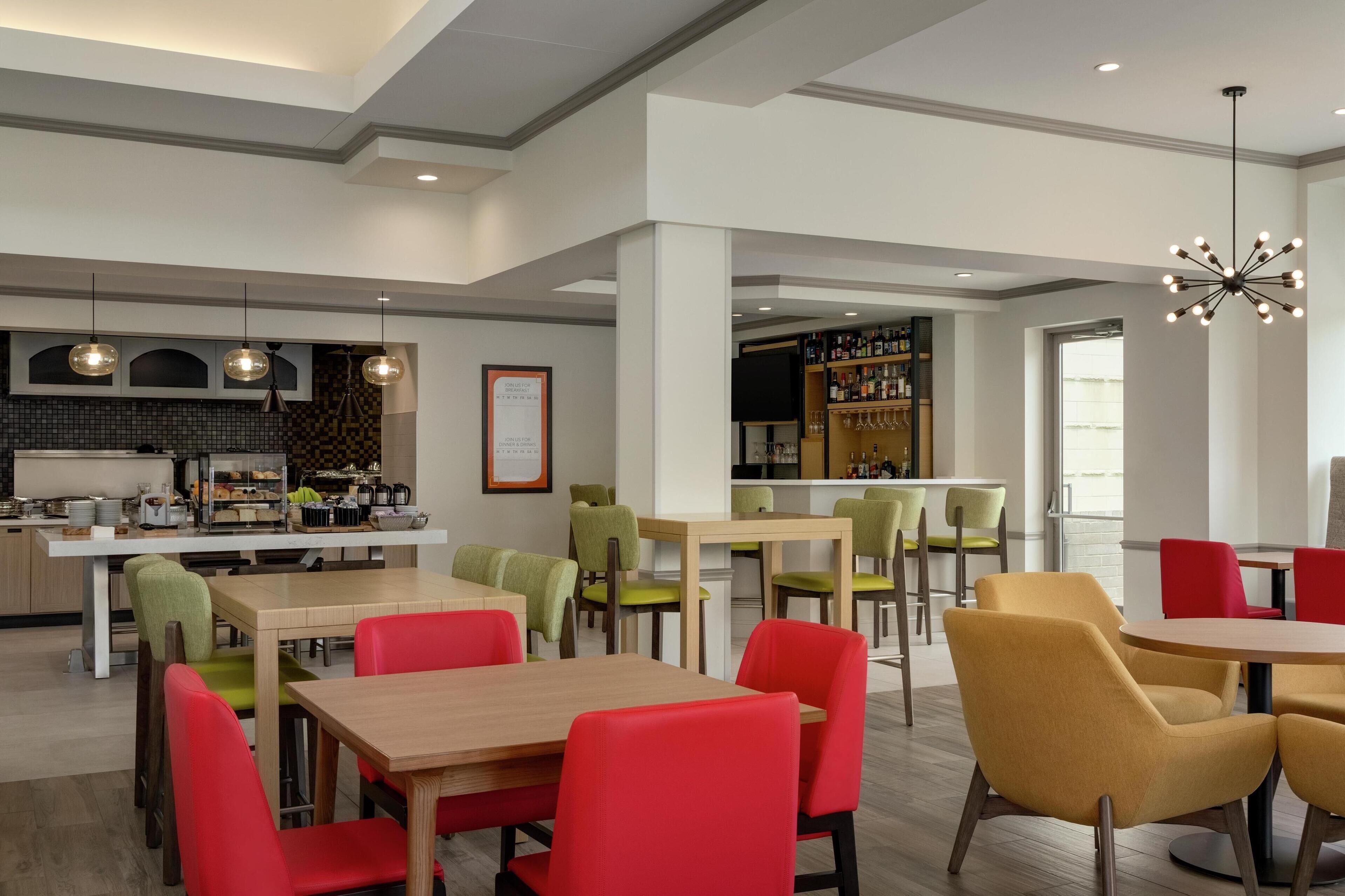 A modern dining area with multiple tables and chairs, a bar area, and a kitchen in the background.