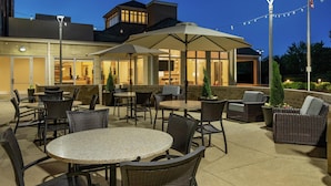 An outdoor patio area with round tables and wicker chairs, featuring string lights and potted plants. - Hilton Garden Inn Cleveland Airport (Cleveland)