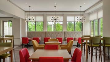 Un comedor moderno con varias mesas y sillas, amplias ventanas con vista a zonas verdes e iluminación colgante.
