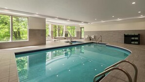 An indoor swimming pool with clear views of trees through large windows, a tiled floor, and a built-in bench area. - Hilton Garden Inn Cleveland Airport (Cleveland)
