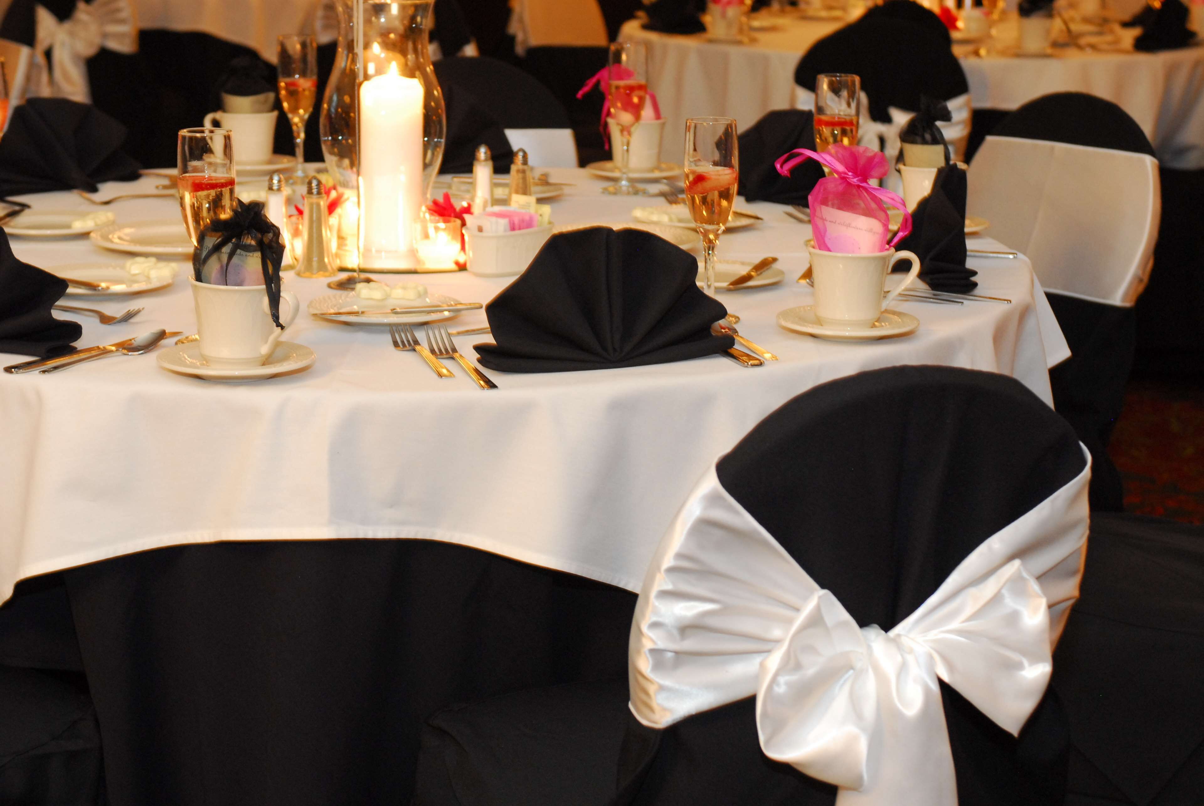 A formal dining table set with white tablecloths, black chair covers, and a large candle centerpiece.