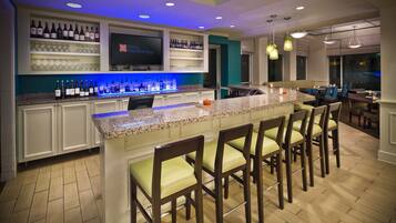 Zona de bar con una barra larga, diversas opciones de asientos y una pantalla mostrando el nombre del hotel.
