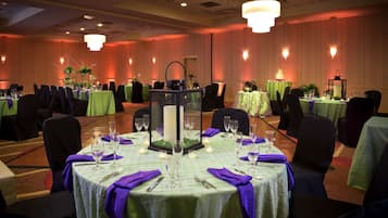 Une salle de banquet où les tables sont dressées pour un événement formel, avec des nappes vertes, des serviettes violettes et des centres de table ornés de bougies.