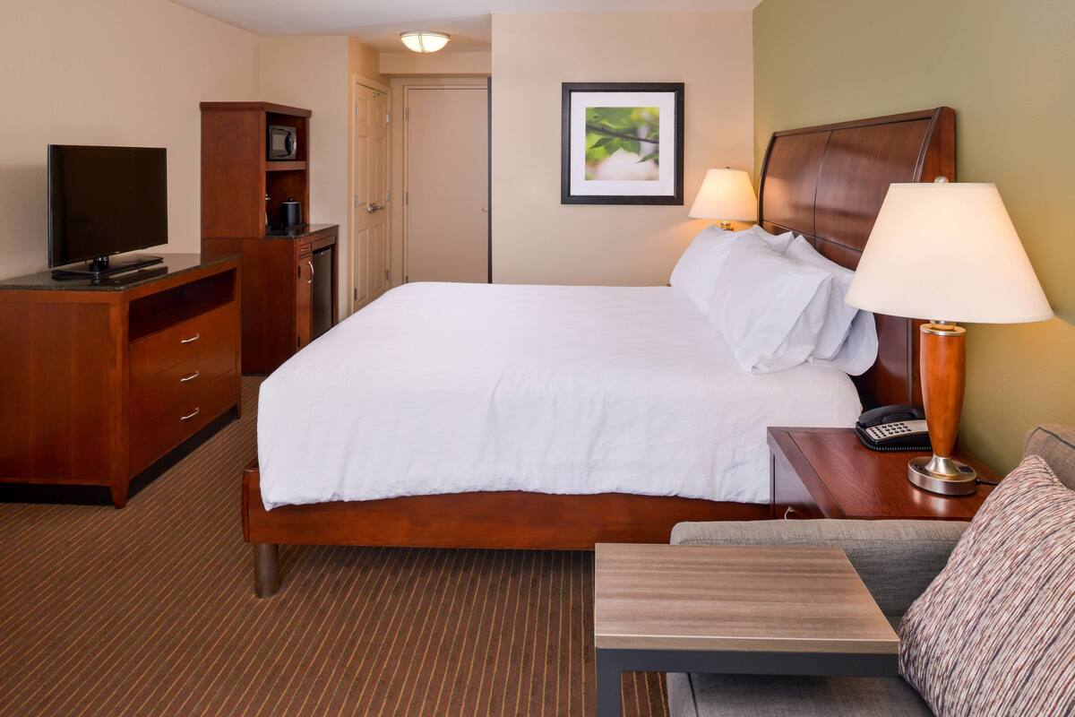 Ein Hotelzimmer mit Bett, Schreibtisch, Fernseher, Lampe und einem gerahmten Bild an der Wand.