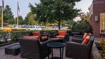 An outdoor seating area with wicker furniture and orange cushions, a small table, and a view of a parking lot and trees.