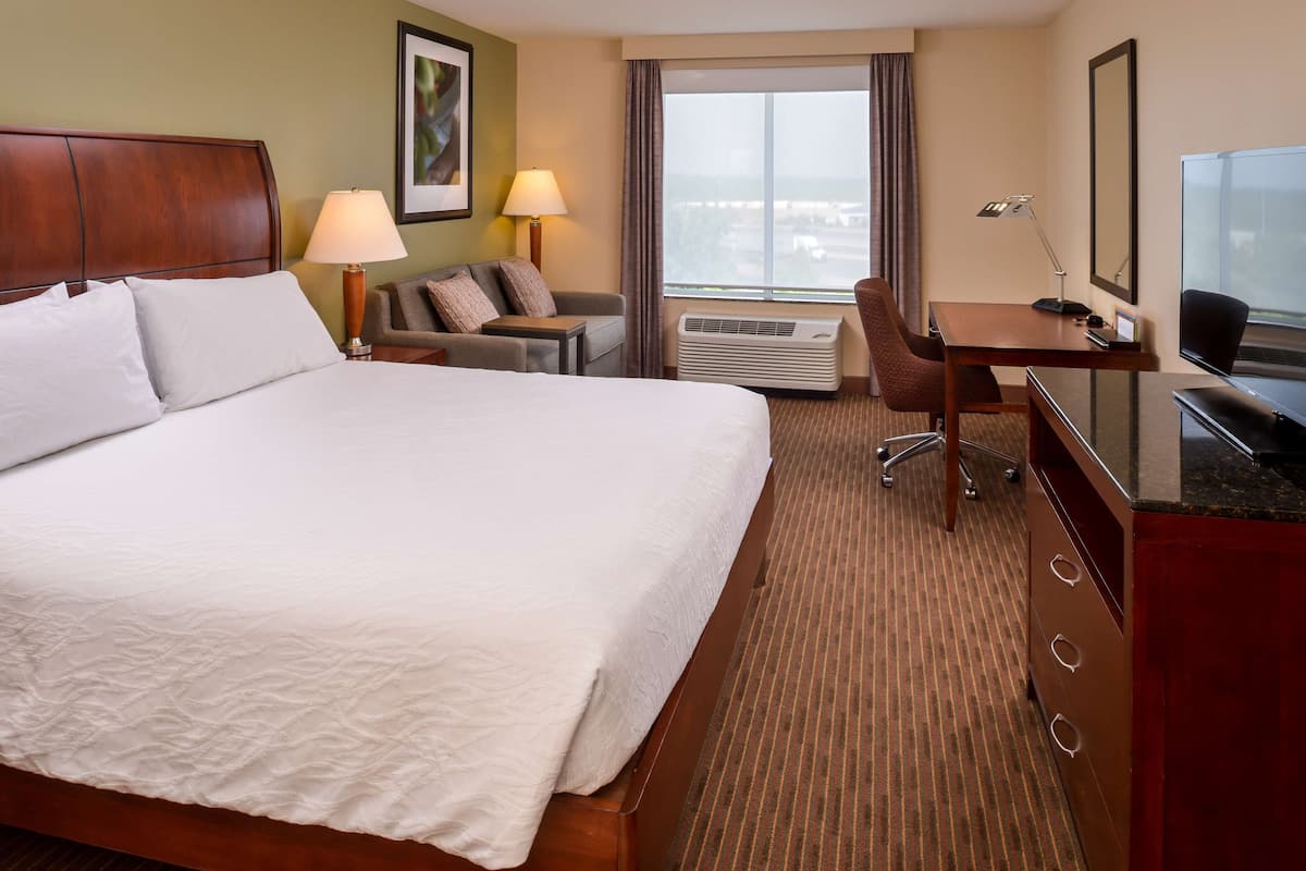 Ein Hotelzimmer mit einem großen Bett, einem Schreibtisch, einem Stuhl, einer Lampe, einer Klimaanlage und einem Fernseher.