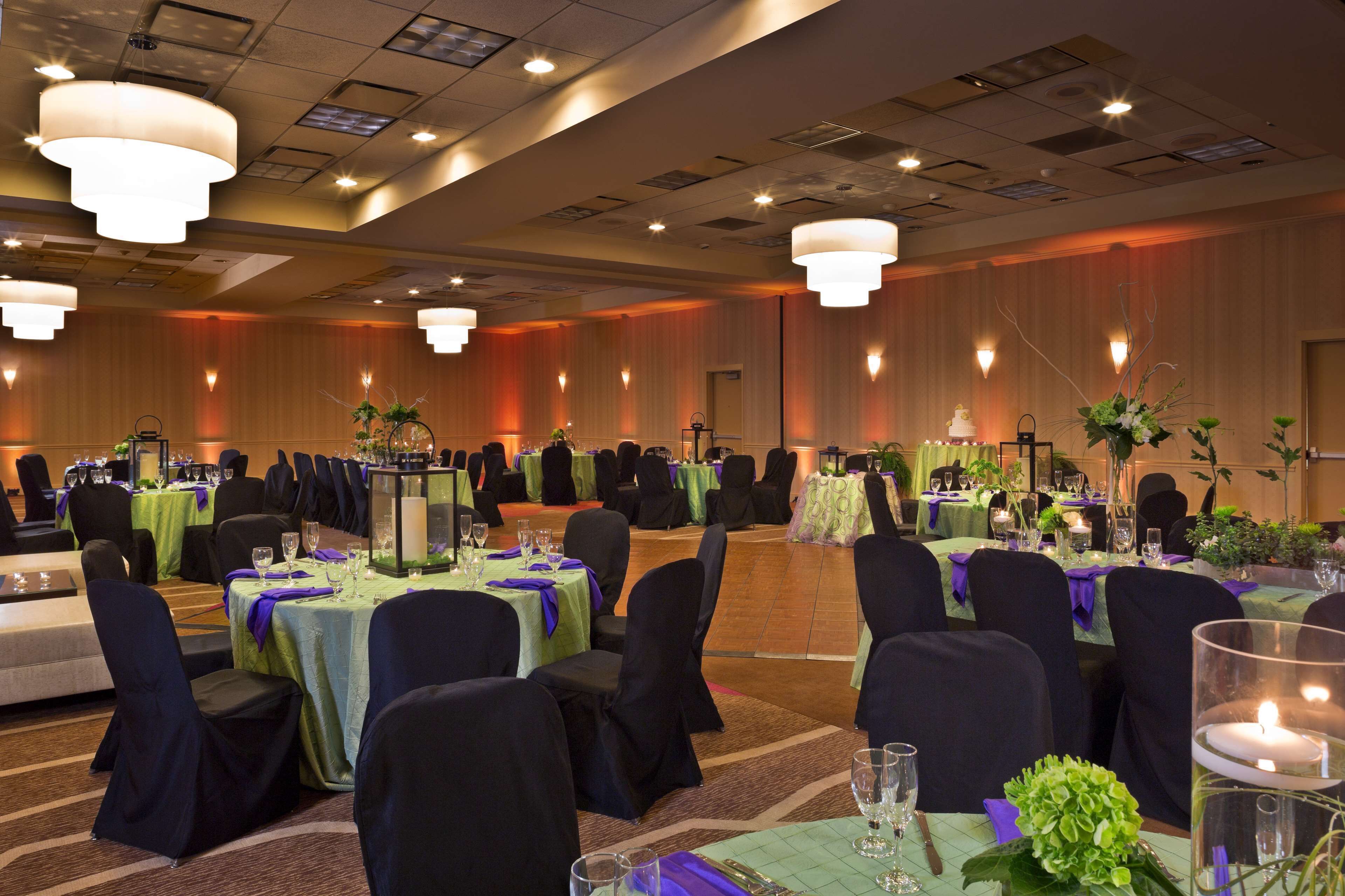A banquet hall with round tables, black chairs, and green tablecloths.