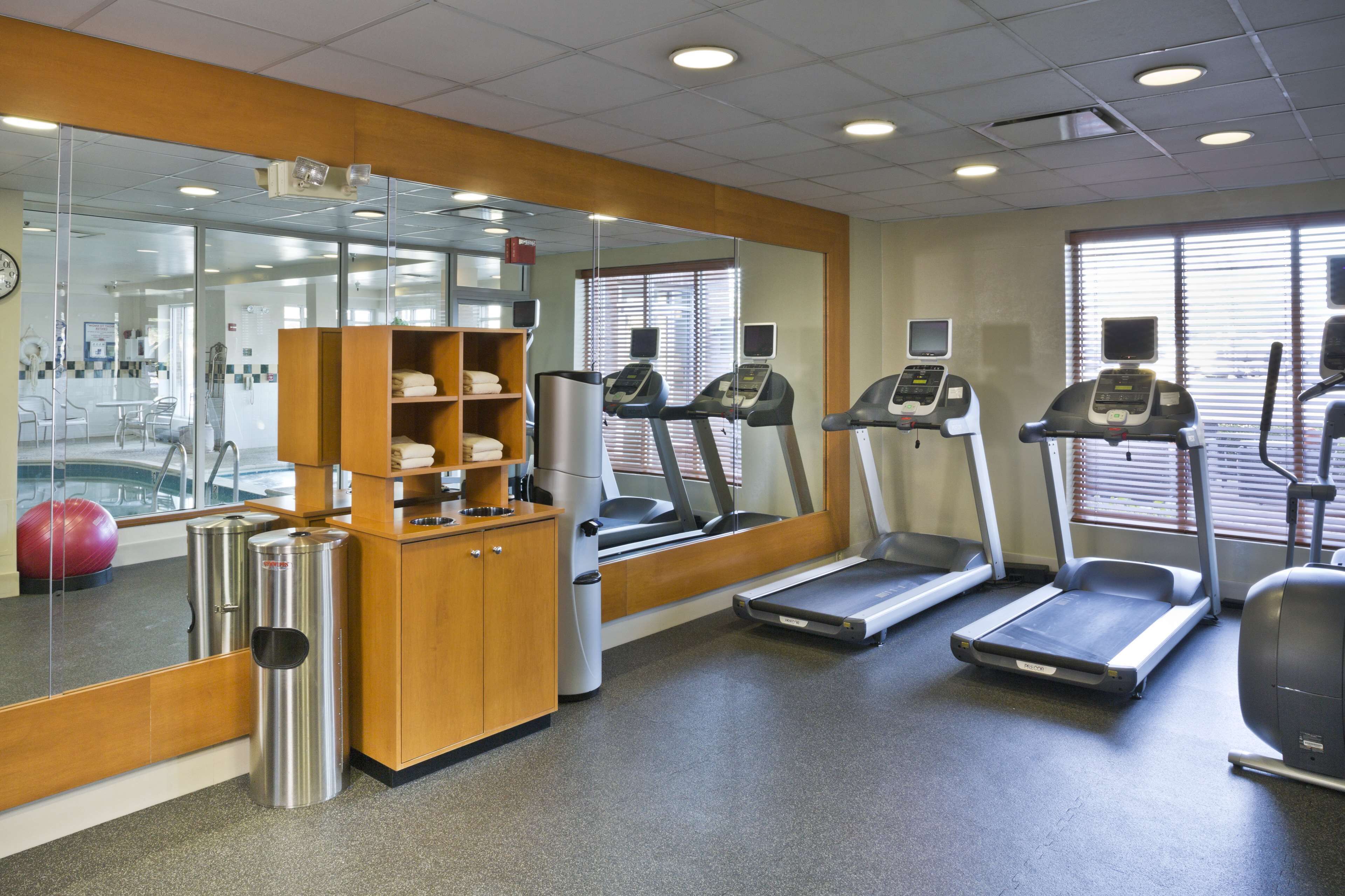 A fitness center with treadmills, a mirrored wall, and a wooden cabinet with towels.
