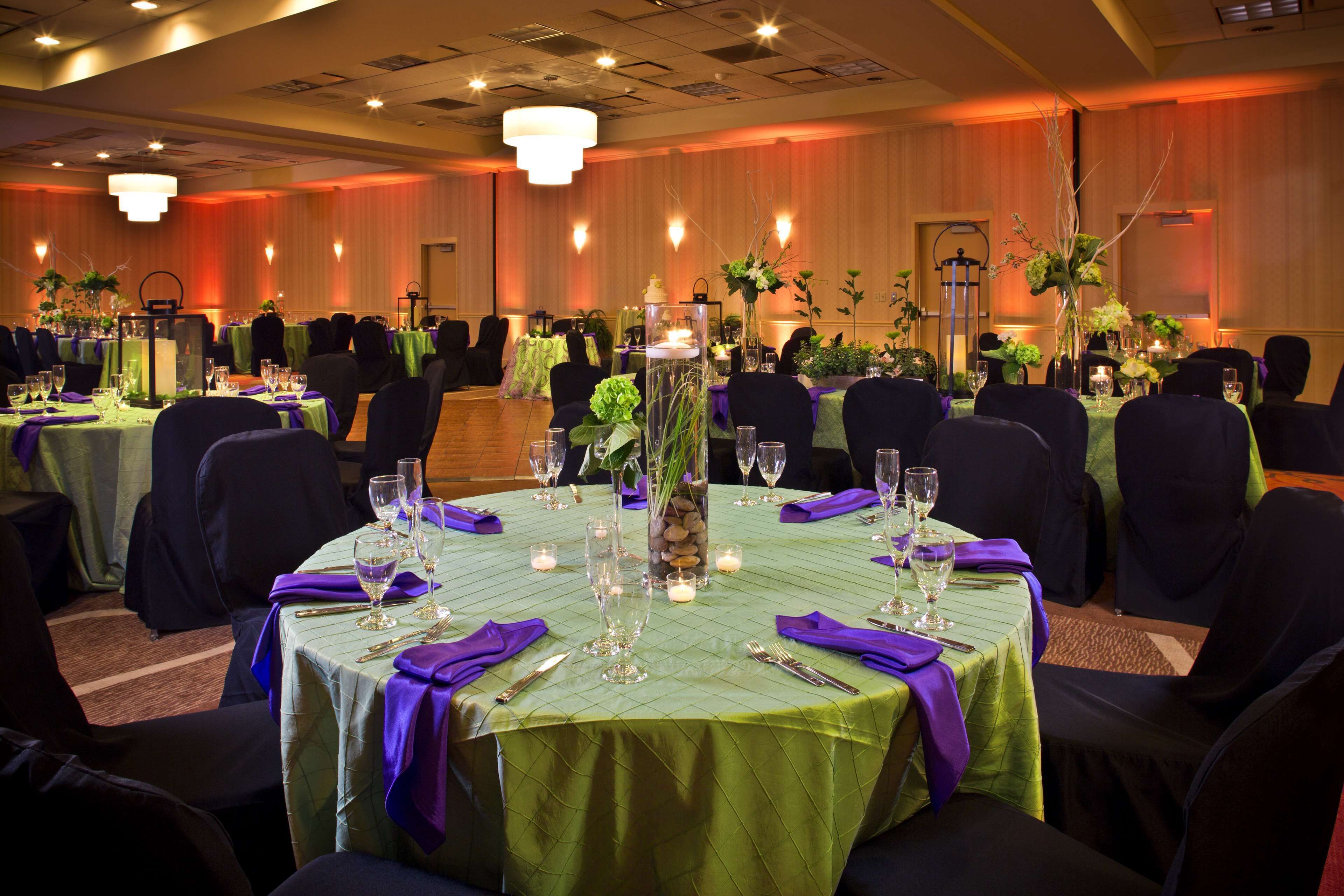 Een feestzaal met ronde tafels, groene tafelkleden, paarse servetten en kaarsdecoraties.