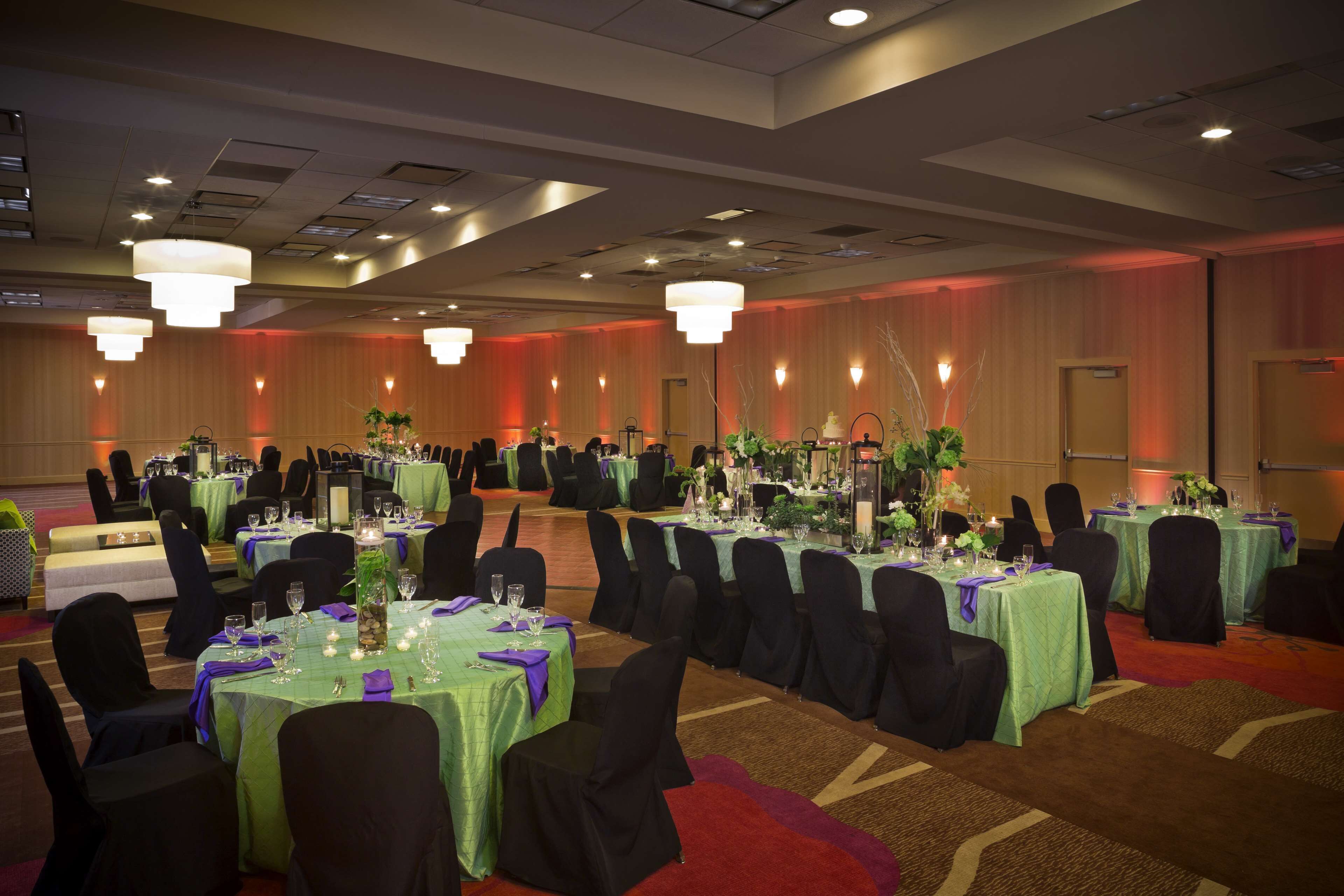 A banquet hall with round tables, black chairs, and green tablecloths.