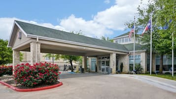 Welcome to our hotel, marked by a covered entrance with a clearance of 10 feet, surrounded by a beautifully landscaped area with flowering bushes.