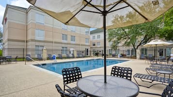 A pool area with lounge chairs and umbrellas, a pool, and a building in the background.