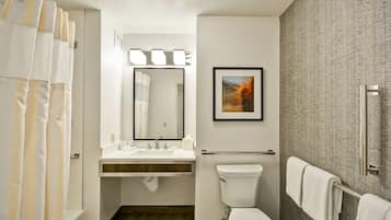 A modern bathroom with a shower curtain, a sink with a mirror, a toilet, and a towel rack.
