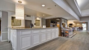 A hotel reception area with a counter, a large decorative light fixture, and a view into the restaurant area. - Hilton Garden Inn Austin/Round Rock (Round Rock)