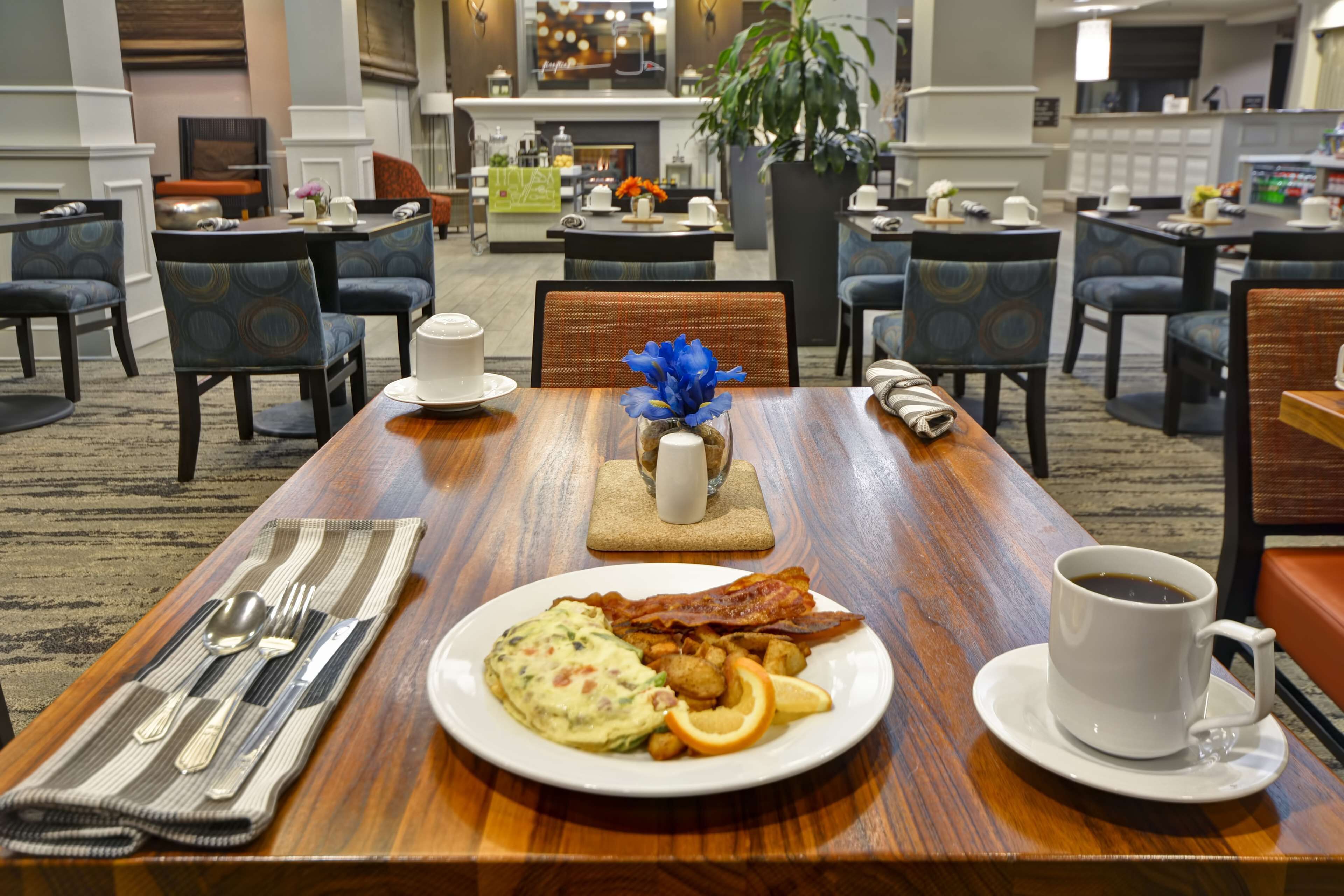 A dining table with breakfast items, including eggs, bacon, and orange slices, and a cup of coffee.