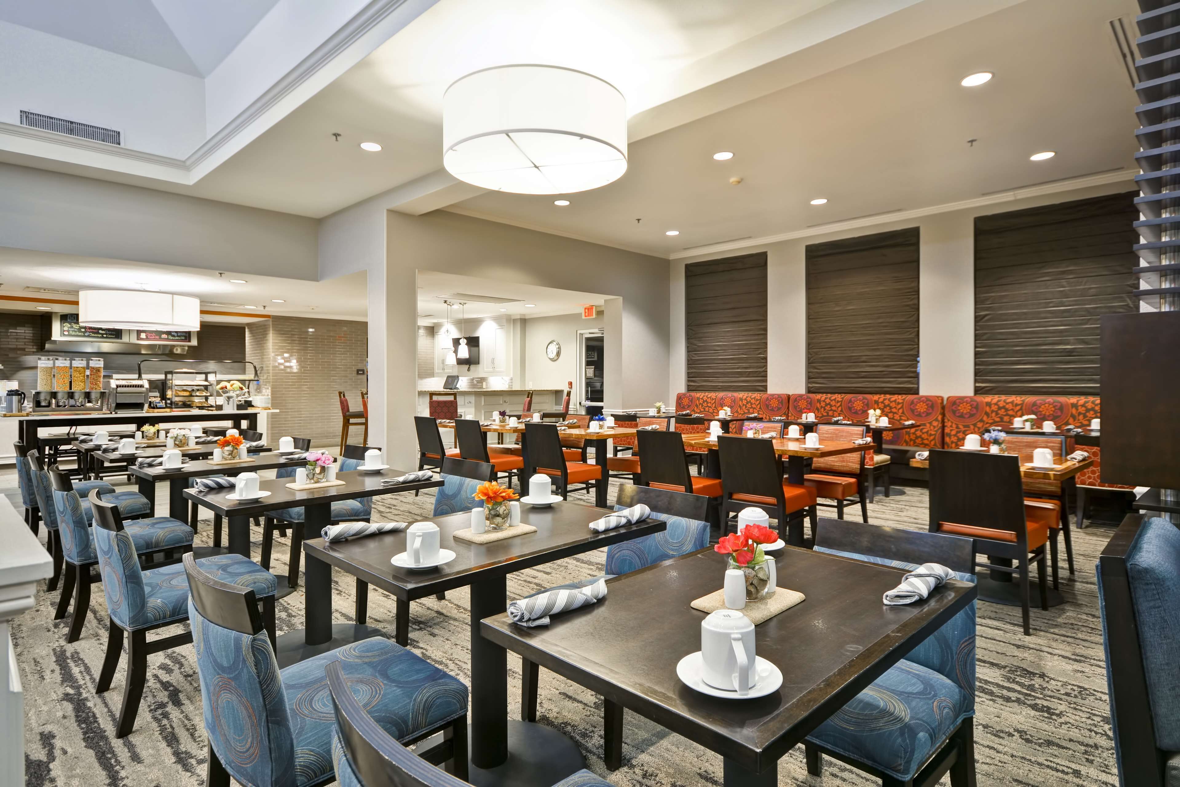 Une salle à manger d’hôtel avec de nombreuses tables et chaises, une cuisine à l’arrière-plan et un grand lustre.
