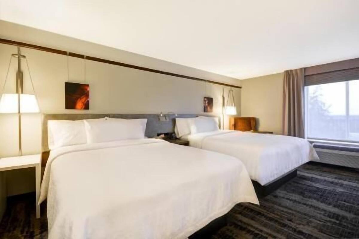 A hotel room with two beds, a large window, and a view of the outdoors.